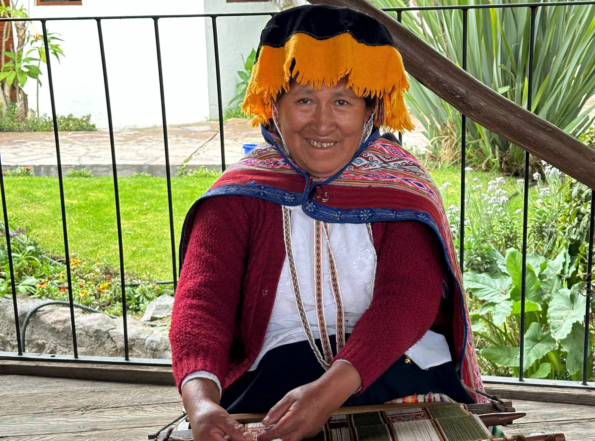 Andean artisan smiling while weaving on a traditional loom