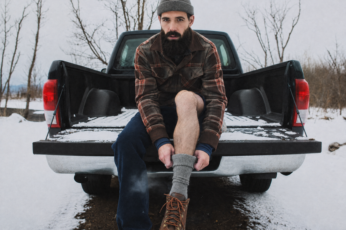 Man pulling on grey alpaca socks before his hiking boots at a snowy trailhead